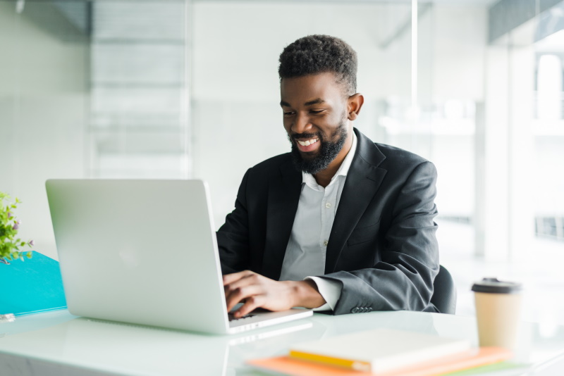 Thoughtful African American businessman wearing glasses using laptop, pondering project, business strategy, puzzled employee executive looking at laptop screen, reading email, making decision